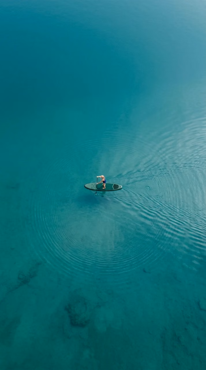 Aerial View of Lone Paddleboarder on Turquoise Lake - Free Mobile AMOLED Wallpaper Background