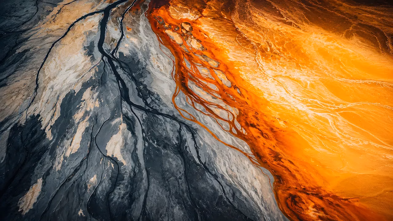 Top-down view of vibrant orange mineral water flowing through dark volcanic sediment.