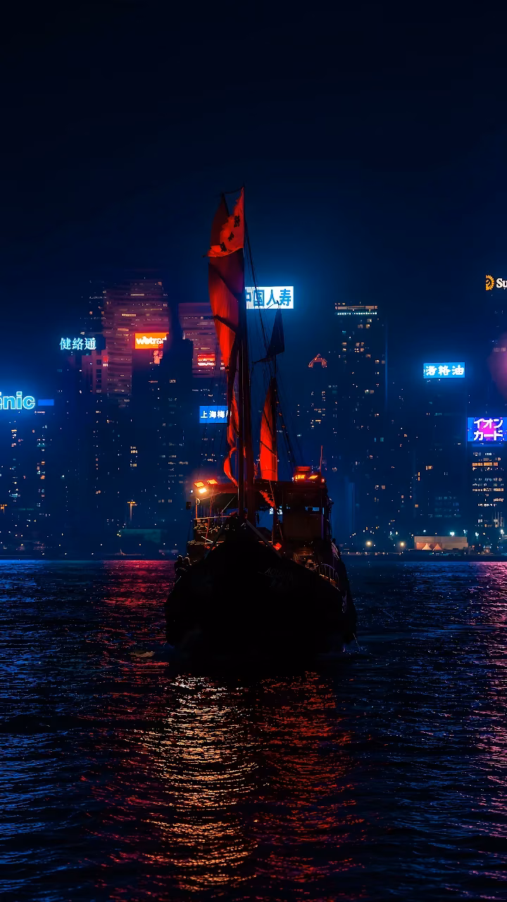 Download Aqua Luna Junk Boat Hong Kong Night 4K Wallpaper in Mobile HD Traditional Chinese junk boat with illuminated red sails on dark harbour water facing glowing city skyscrapers.