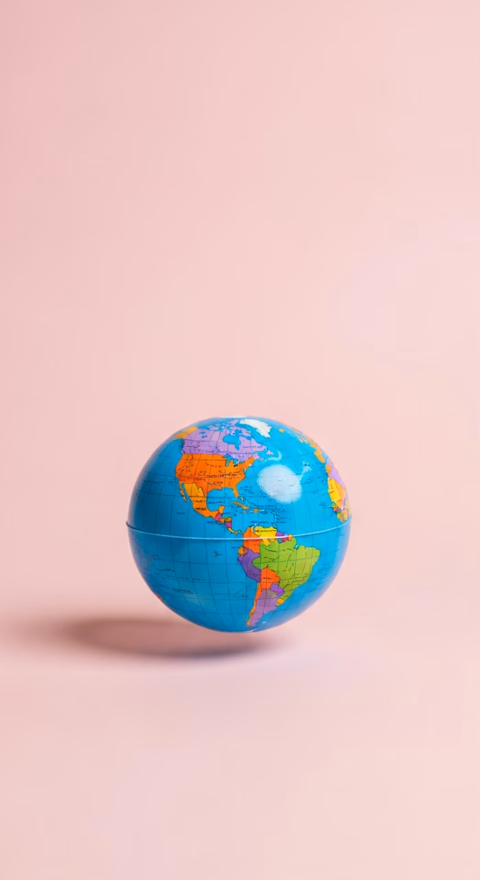 Bright Studio Shot of a Small Colorful World Globe on a Solid Pastel Pink Background - Free Mobile AMOLED Wallpaper Background