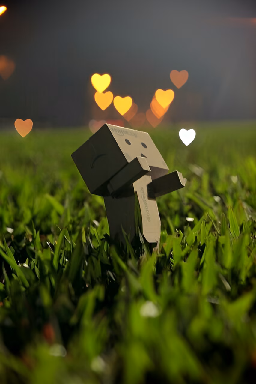 Cardboard Robot in Grass with Floating Heart Bokeh Lights - Free Mobile AMOLED Wallpaper Background