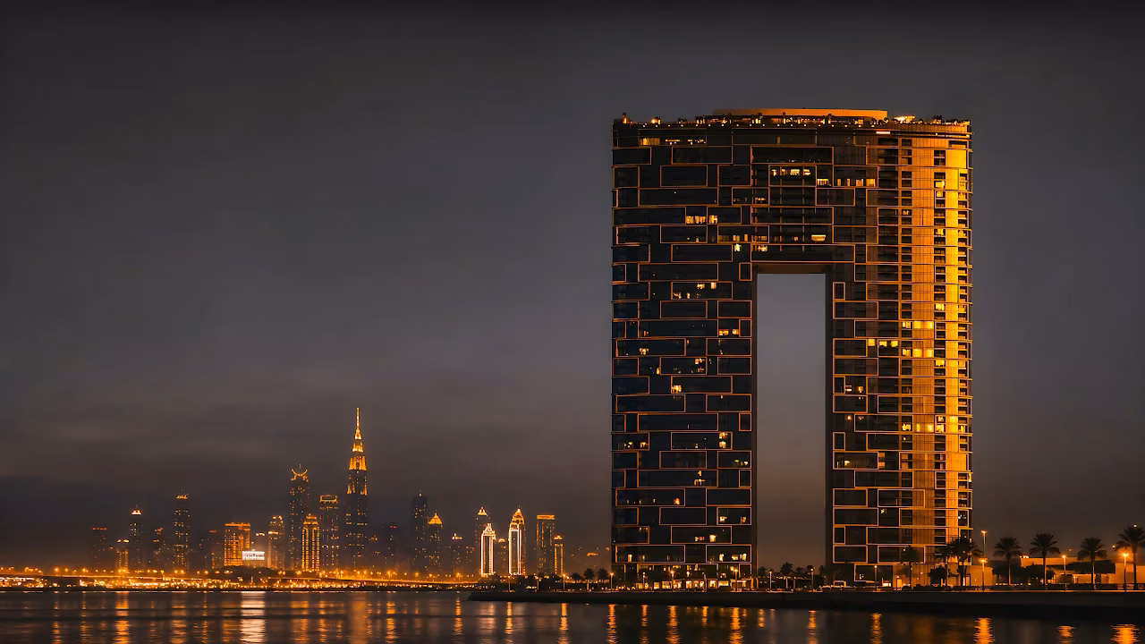 Address Beach Resort arch skyscraper illuminated at night across the water with the Dubai skyline.