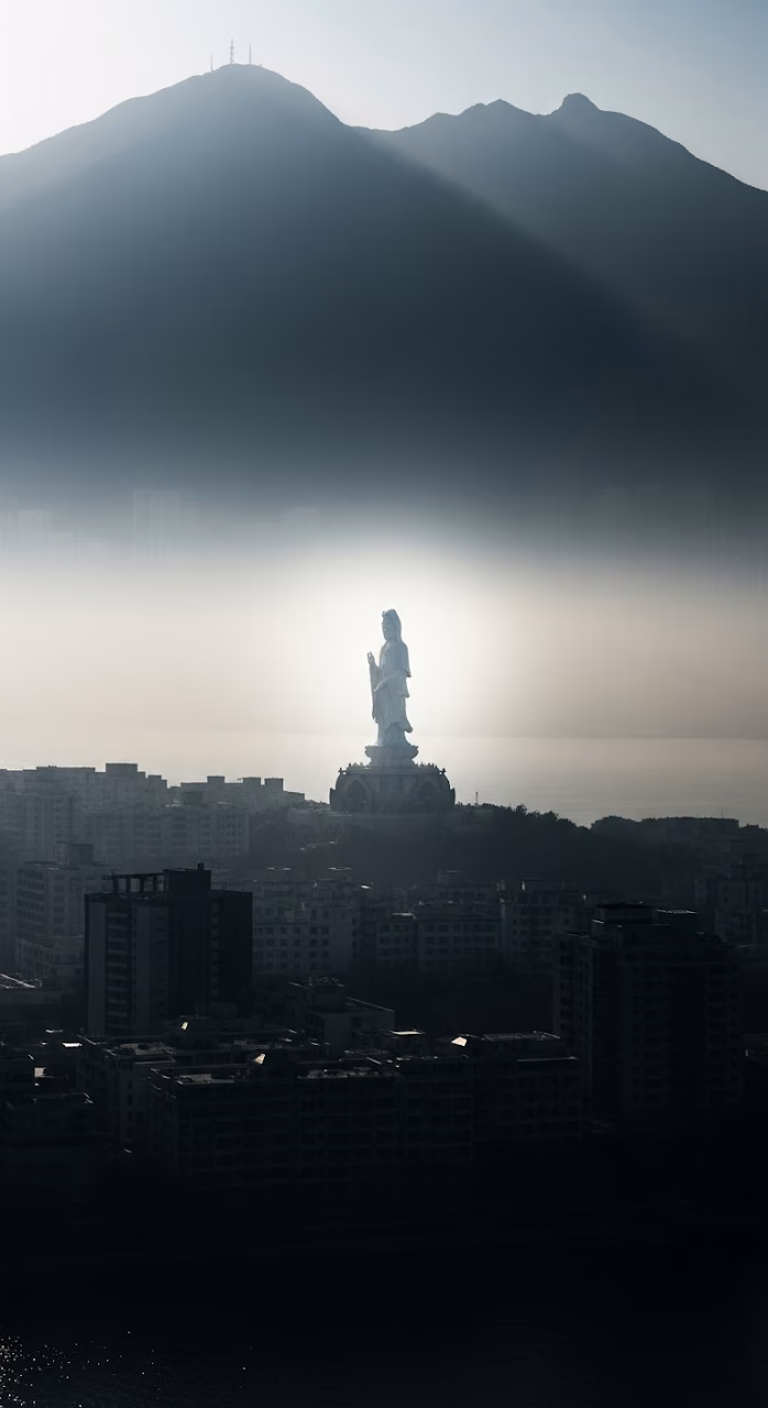 Ethereal View of a White Guanyin Statue Floating Above a Silhouetted Cityscape and Misty Mountains - Free Mobile AMOLED Wallpaper Background