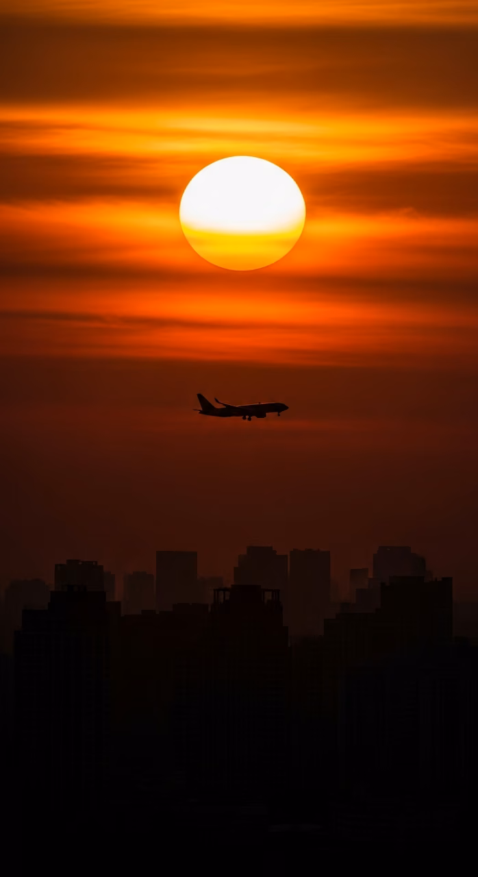 High-Contrast Telephoto Silhouette of an Airplane and City Skyline Against a Fiery Orange Sunset - Free Mobile AMOLED Wallpaper Background