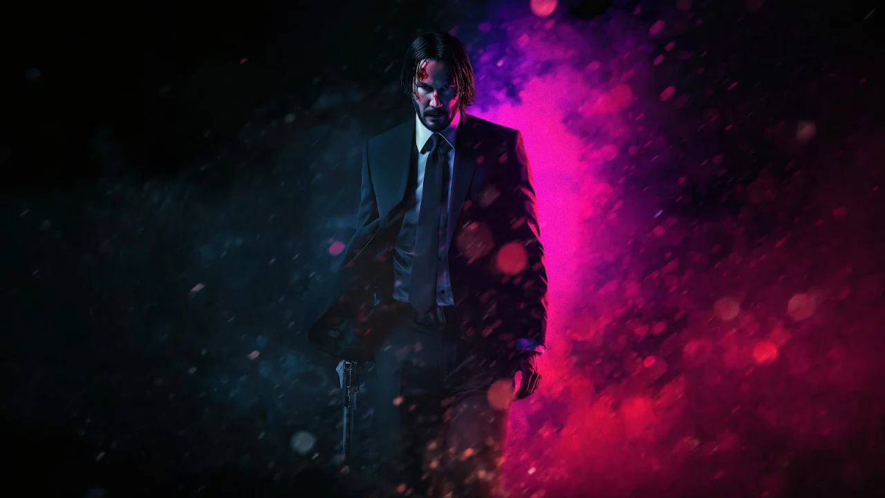 John Wick in a black suit walking forward through heavy rain illuminated by neon pink and cyan blue lights.