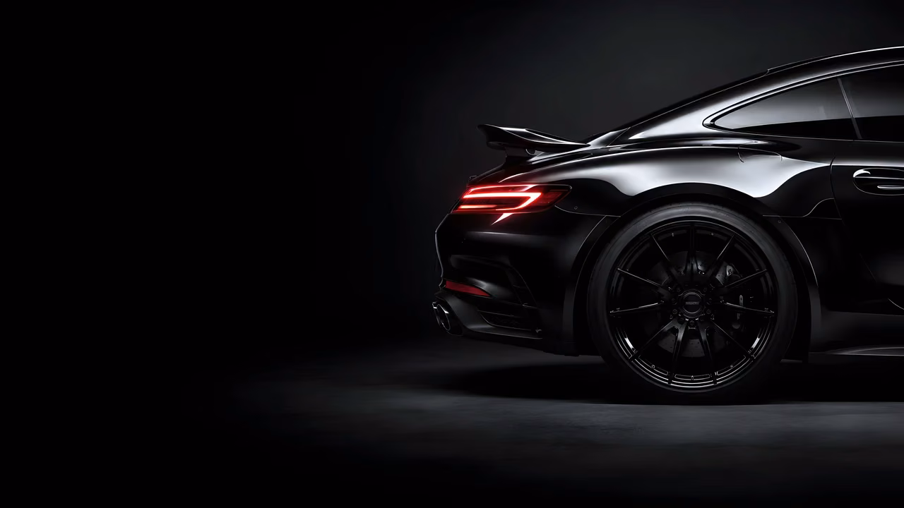 Glossy black high-end sports car rear quarter panel showcasing curved bodywork and a sleek red light bar against a dark gray backdrop.