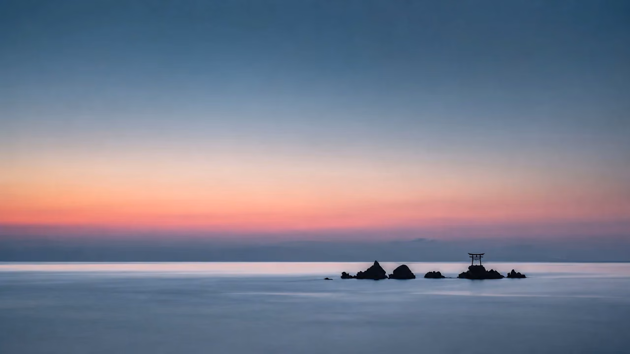 Download Torii Gate Ocean Rock Sunset Minimal 4K Wallpaper in 4K UHD Small black torii gate perched on offshore rocks in calm blue ocean water beneath a pink sunset gradient sky.