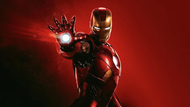Iron Man aims an activated repulsor blast forward against a solid red studio background. Iron Man in red and gold armor with glowing eyes and chest reactor, aiming a white repulsor hand beam on a red background.