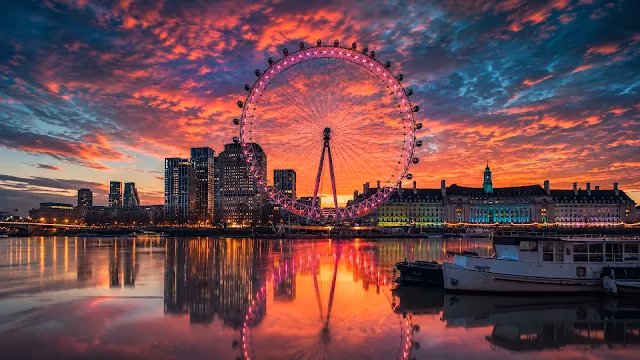 The London Eye glows magenta over the River Thames during a dramatic crimson sunset. London Eye illuminated in pink, reflecting on the calm River Thames under an orange and purple sunset sky.