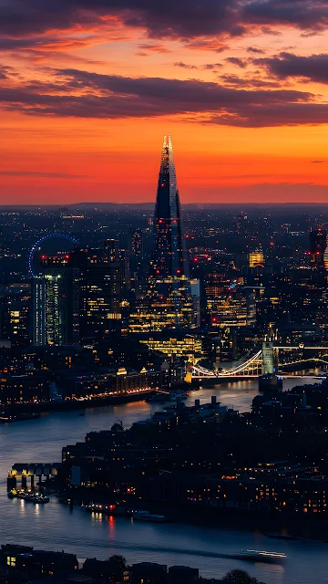 The Shard and Tower Bridge illuminate the London skyline beneath a fiery red evening sky. Aerial view of The Shard, Tower Bridge, and River Thames under a red and orange twilight sky.