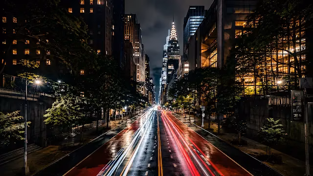 Long exposure photo of red and white car light trails on a New York City street facing the Chrysler Building.