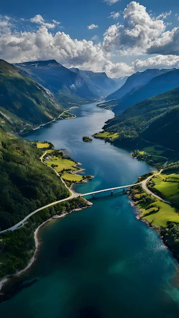 Aerial view of a turquoise fjord flanked by steep green mountains and crossed by a road bridge in Norway. Aerial view of a blue fjord surrounded by green mountain slopes and connected by a road bridge in Norway.