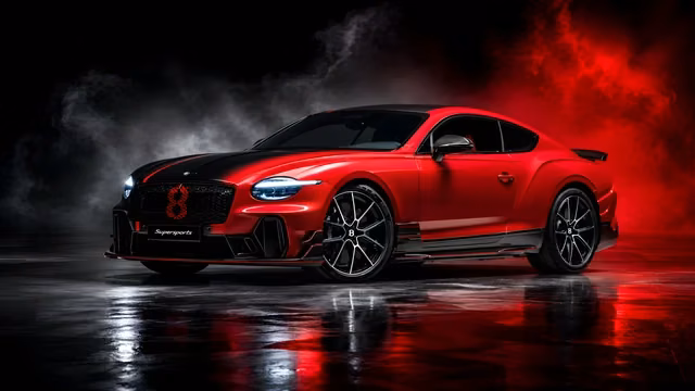 Red and black performance coupe parked on a reflective floor in a dark studio.