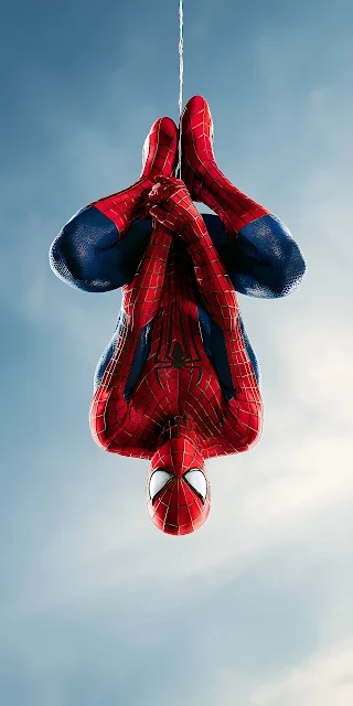 Spider-Man hangs inverted from a single web line against a clear open daylight sky. Spider-Man hanging upside down on a web line against a clear blue sky wearing a red and blue textured suit.