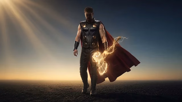 Thor in armor and a red cape walking forward on a dark field while holding an electrified glowing hammer under sunlight.