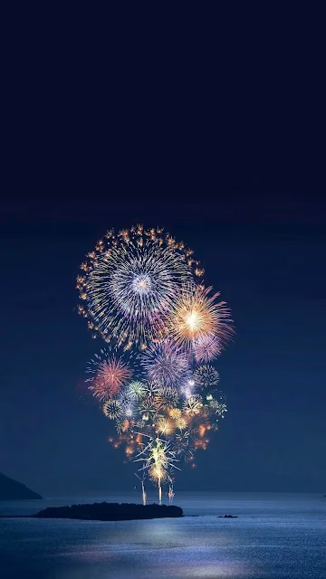 Vibrant Fireworks Bursting Over Dark Ocean Island - Free 4K & 8K Mobile Wallpaper